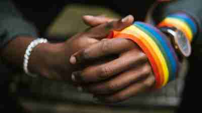 Closeup of a person's hands wrapped in an LGBTQ ribbon.