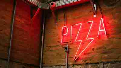 A neon "pizza" sign hanging on a restaurant wall. Dining out can be tricky for families raising autistic children.