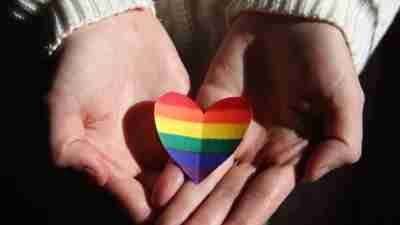 Rainbow pride heart placed in the palms of two hands.