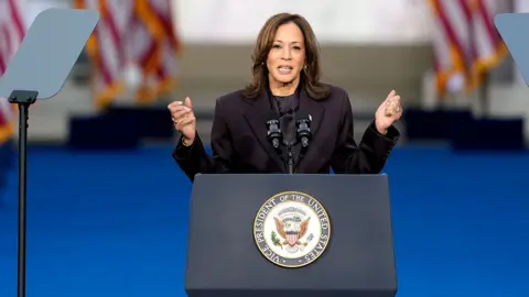 Kamala Harris holds her hands out as she looks at camera while speaking at a lecturn on 6 November