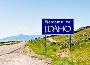 Blue Welcome to Idaho road sign next to road with mountains in the background