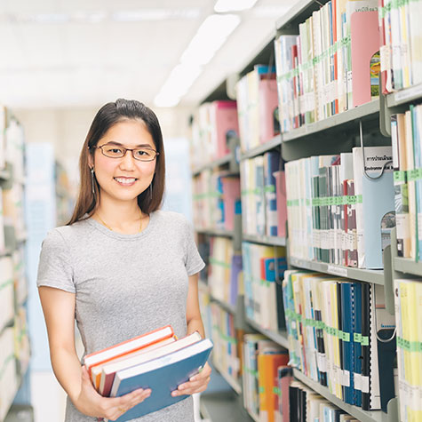 A young woman holding books in library stacks