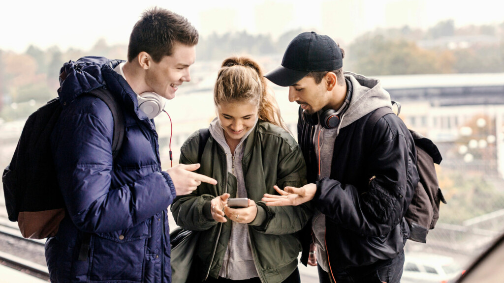 En grupp ungdomar står på perrongen och tittar tillsammans på en mobil. Meta samlar in stora mängder data om dig för att använda vid riktad annonsering.