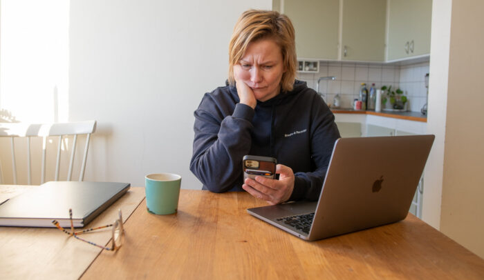 Ledsen person tittar på sin mobil, sittandes vid ett köksbord.