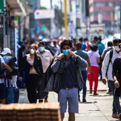 People walk down the sidewalk in a city - most are wearing face masks.