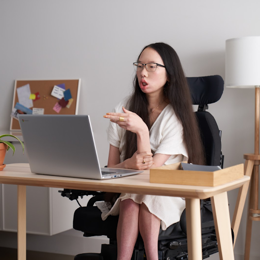 Googler Aubrie Lee (she/her) sits in her wheelchair and takes a meeting at a desk