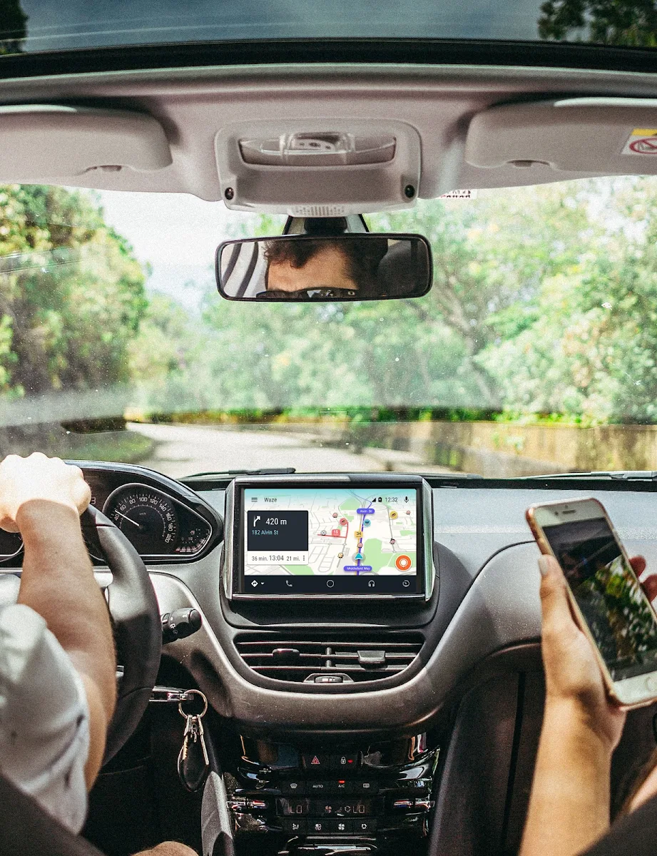 A view of a dashboard from the rear seats. Waze can be seen on the screen and a hand at 2 o'clock on the steering wheel.