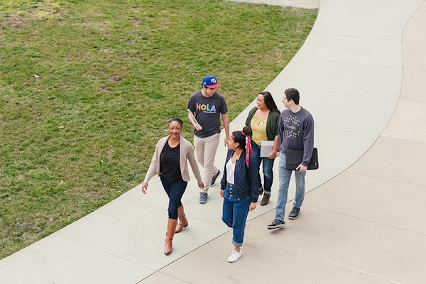 Five Googlers, three of whom are holding laptops, chat and walk down a pathway together