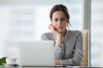 Female office worker wears a black nad white stripe blouse and looking skeptically at her laptop.