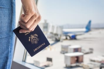 Woman waiting in the airport looking outside holding a passport in her hand.