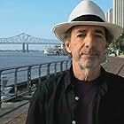 Harry Shearer, director of The Big Uneasy, in New Orleans on the bank of the Mississippi River with the Pontchartrain Expressway in the background.