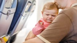 Young tired father and his crying baby daughter during flight on airplane going on vacations.