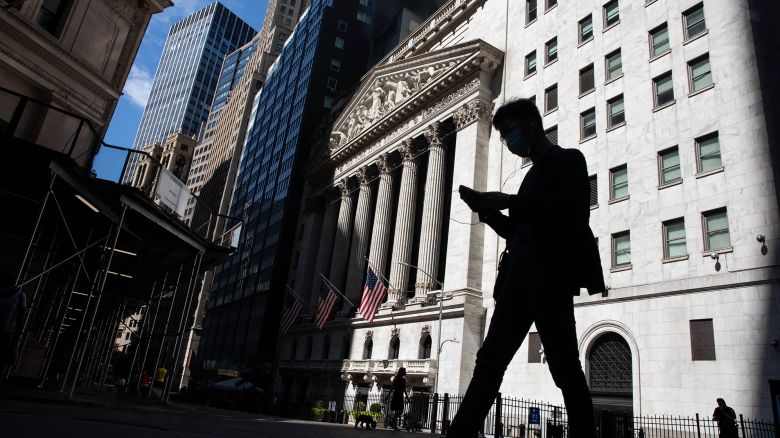 A pedestrian wearing a face mask looks at a smartphone while passing in front of the New York Stock Exchange (NYSE) in New York, U.S., on Monday, July 20, 2020. 