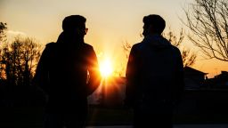 Two handsome casual trendy young men, 2 friends, in an urban park walking and chatting together