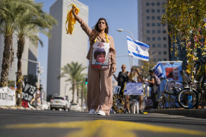 A woman with a photograph of a child who was abducted during the Hamas attack on Israel hands out yellow ribbons to passing drivers in central Tel Aviv, Israel, on October 25.<br /