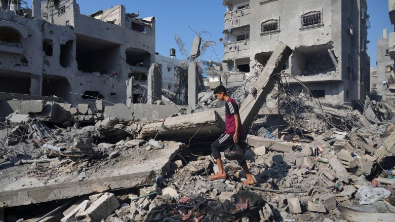 Palestinians stand by the building destroyed in an Israeli airstrike in Deir al-Balah, south of the Gaza Strip, Saturday, Oct. 14, 2023. (AP Photo/Hatem Moussa)