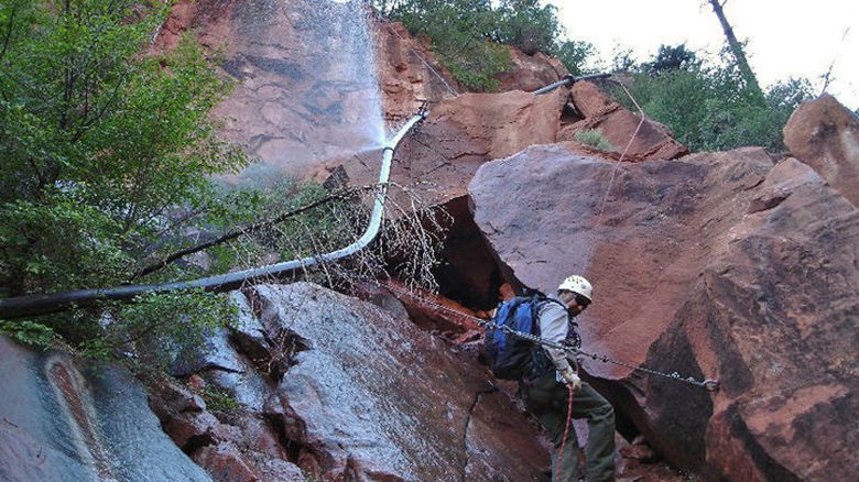 FILE - In this undated photo provided by the National Park Service shows a water spraying from a break in an exposed section of the Grand Canyon trans-canyon waterline as a worker attempts repairs. (National Park Service via AP, File)