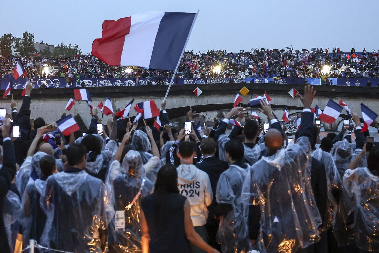 French athletes wave flags as they sail in a boat on the river Seine.