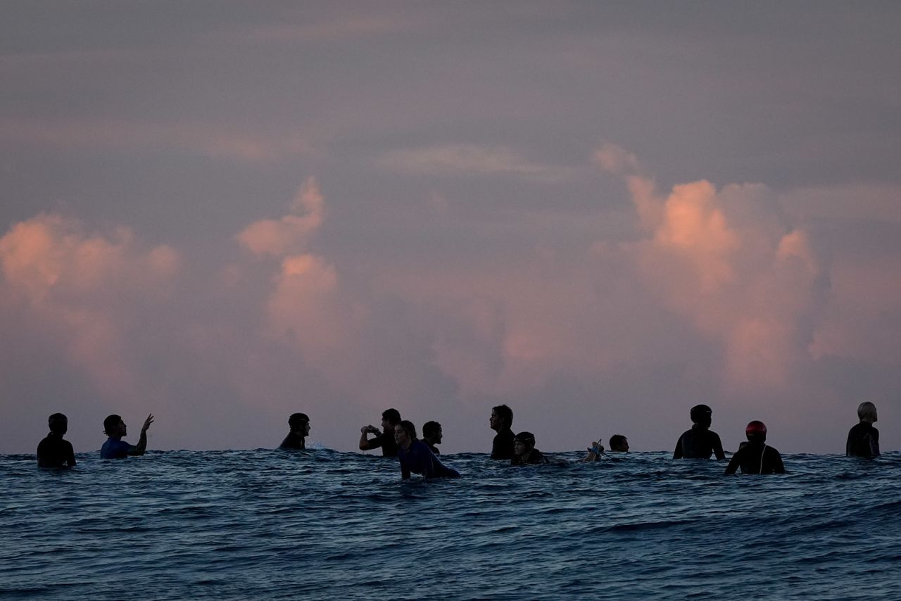 Surfers talk in the lineup before the start of the third round of surfing competition on July 29.