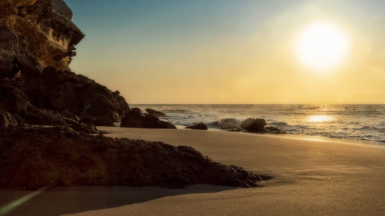 Beautiful sunset on the deserted Namibe beach. Photograph taken near the ground with cliff and rocks. Africa. Angola.