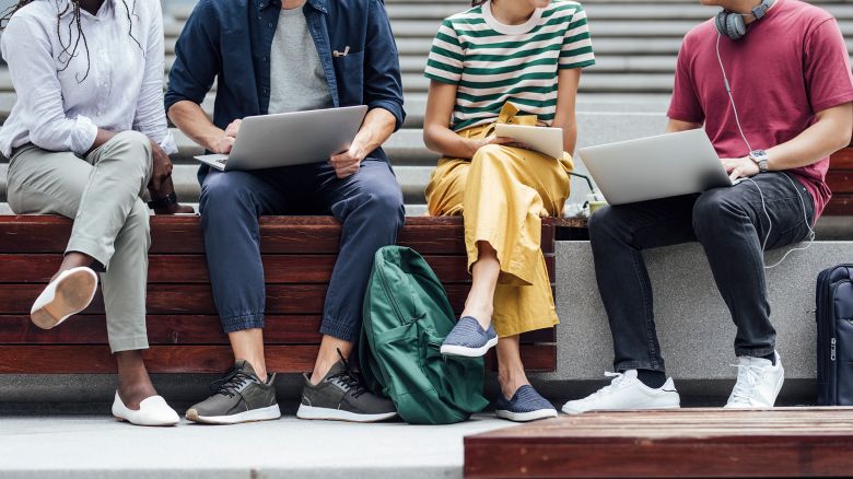 Group of cropped unrecognisable university students sitting outdoors and holding laptops