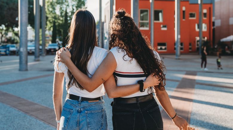 Two friends are shopping together in the city. Rear view of the friends embracing together.