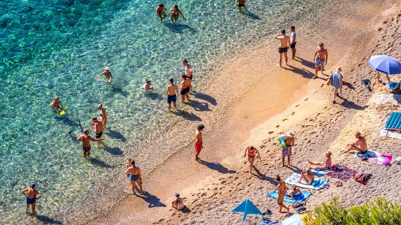 Calella de Palafrugell, Spain - July 10, 2022: Birds eye view of beach with many people sunbathing on sand and swimming.