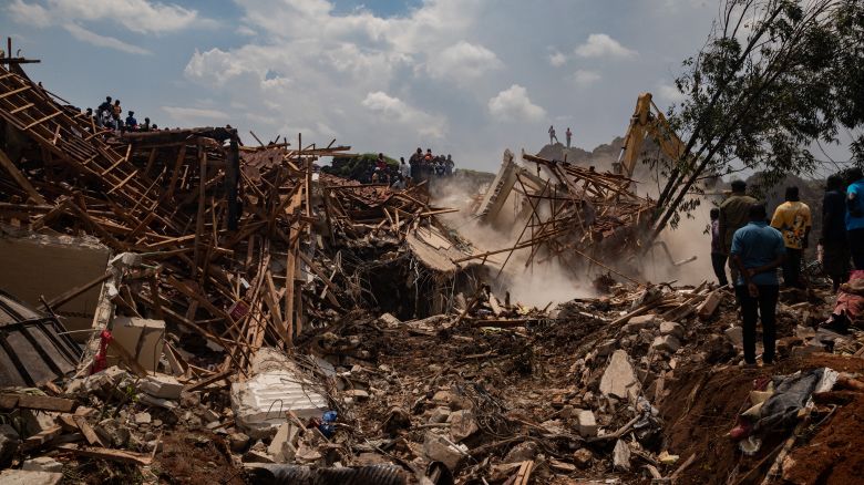 People look on as an excavator helps search for people trapped under debris after a landfill collapsed in Kampala on August 10, 2024. Eight people including two children were killed when a landfill in the Ugandan capital Kampala collapsed, the city authority said.