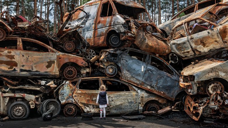 A young girl looks at a pile of destroyed cars left behind in Irpin, Ukraine, after Russia’s invasion of the country in 2022.