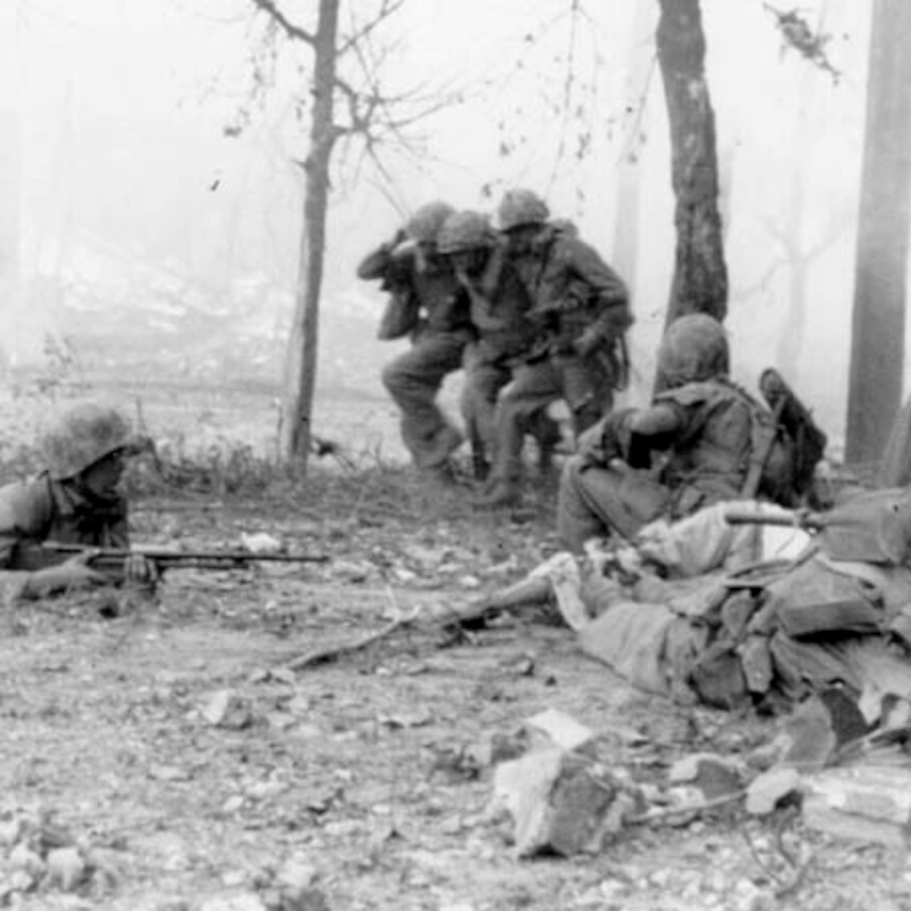 Two soldiers carry an injured soldier while three soldiers lay down on the ground to provide cover fire.