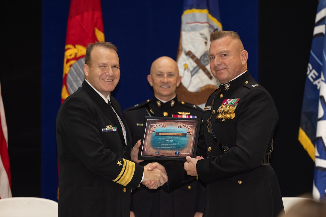 U.S. Navy Rear Adm. Thomas J. Anderson, (left) Program Executive Officer, Ships, presents plaque to U.S. Marine Corps Col. Raymond Feltham, (right) Prospective Program Manager, Medium Landing Ship, as U.S. Marine Corps. Brig. Gen. Robert Brodie, Director of Expeditionary Warfare, Office of the Chief of Naval Operations, looks on during an establishment ceremony for the Medium Landing Ship (LSM) Program Office at the Humphrey's Building on Washington Navy Yard, D.C., Oct. 24, 2024. Col. Feltham's position as a program director is unique in that a Marine will lead a Navy program office. (U.S. Marine Corps photo by Lance Cpl. Joshua Bustamante)