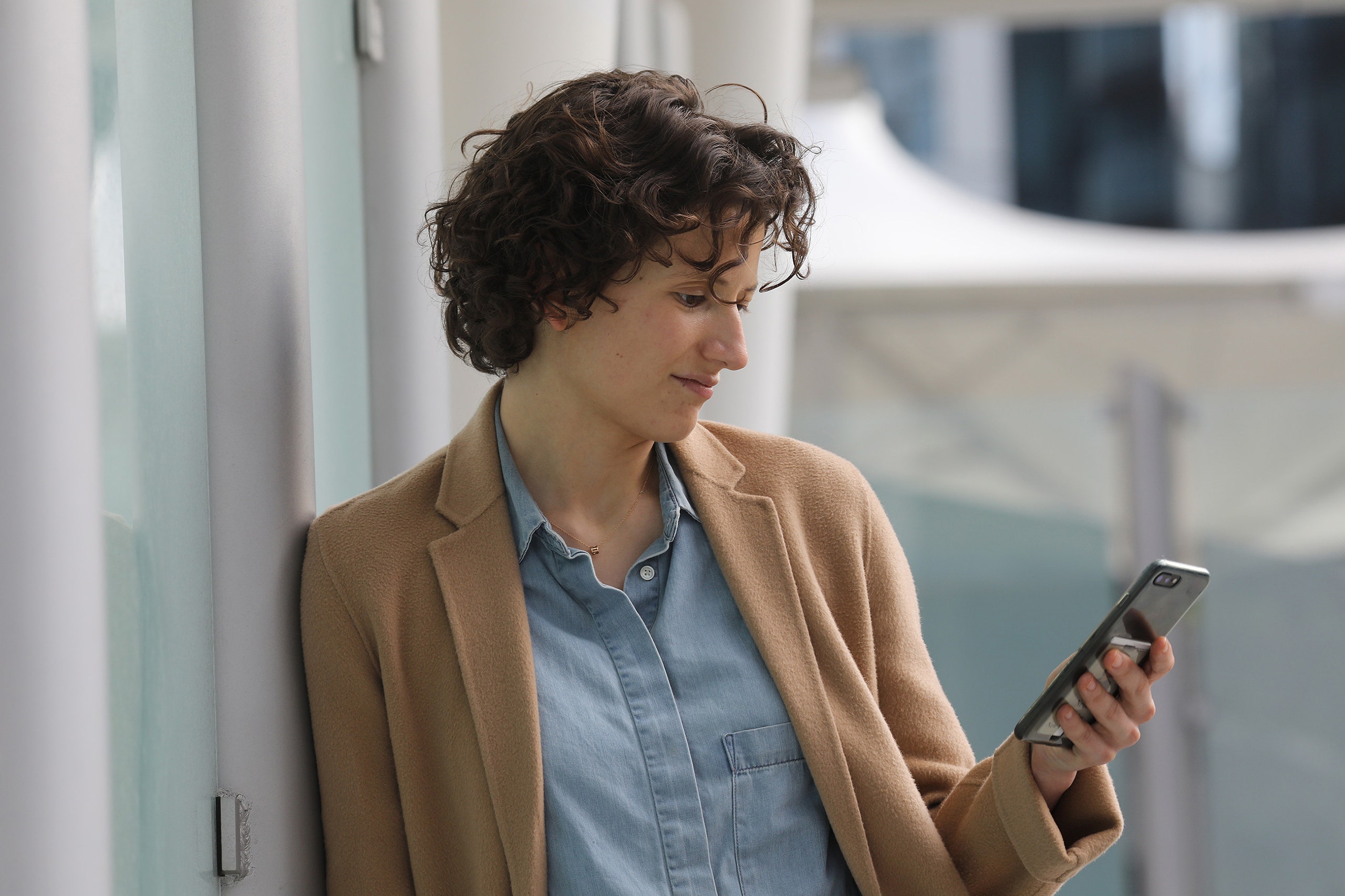 A photo of Nellie Bowles who is wearing a tan blazer over a blue shirt looking at her phone.