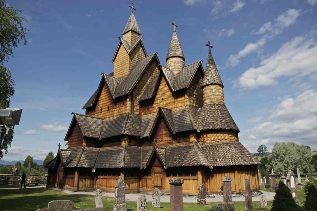 Fotografi av en stor stavkirke. Den er bygget av tre og har mange tak og utspring. Den har tre tårn, og på hvert tårn er det et kors. Foran kirken ser man en kirkegård med gravsteiner.