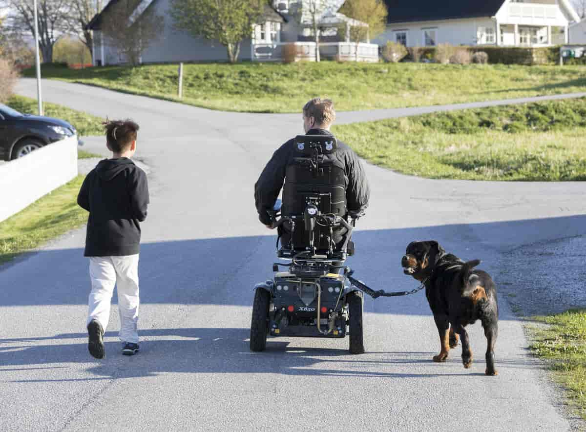 Foto av mann i rullestol, som er på tur med sonen og hunden sin