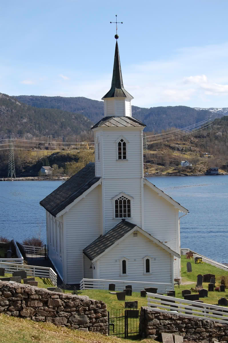 En hvit trekirke som ligger på en gressplen med gravsteiner. Den er enkel, med et klokketårn foran.