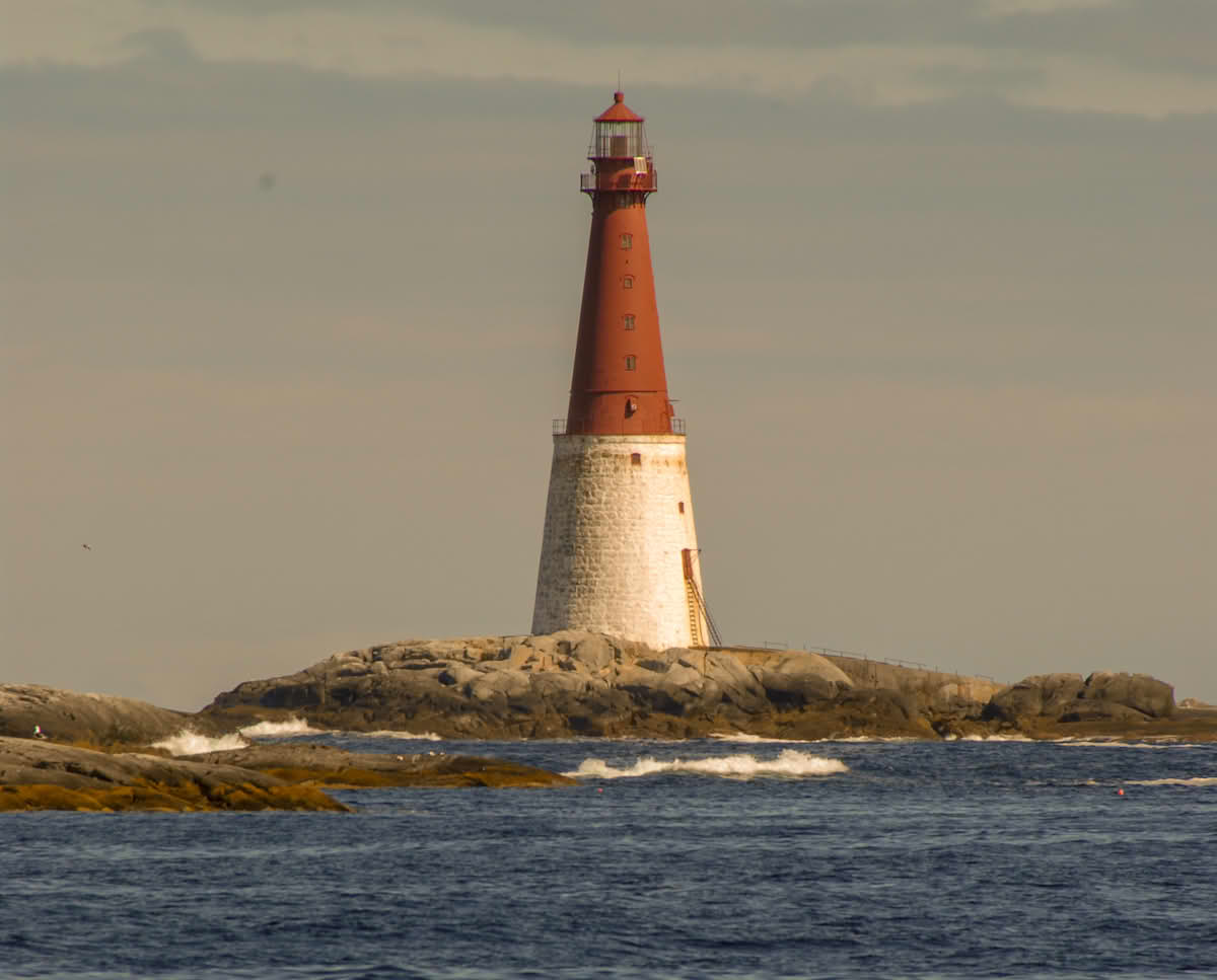 Et rødt og hvitt fyrtårn som står på steingrunn som stikker opp fra havet. 