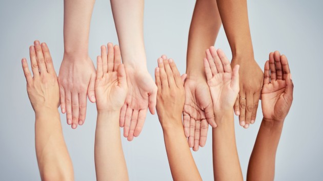 Hands and arms of multiple skin shades facing up and down, touching, in a row.