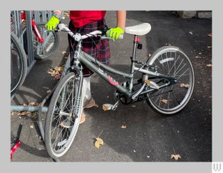 Small grey manual bike being held by someone wearing neon green gloves