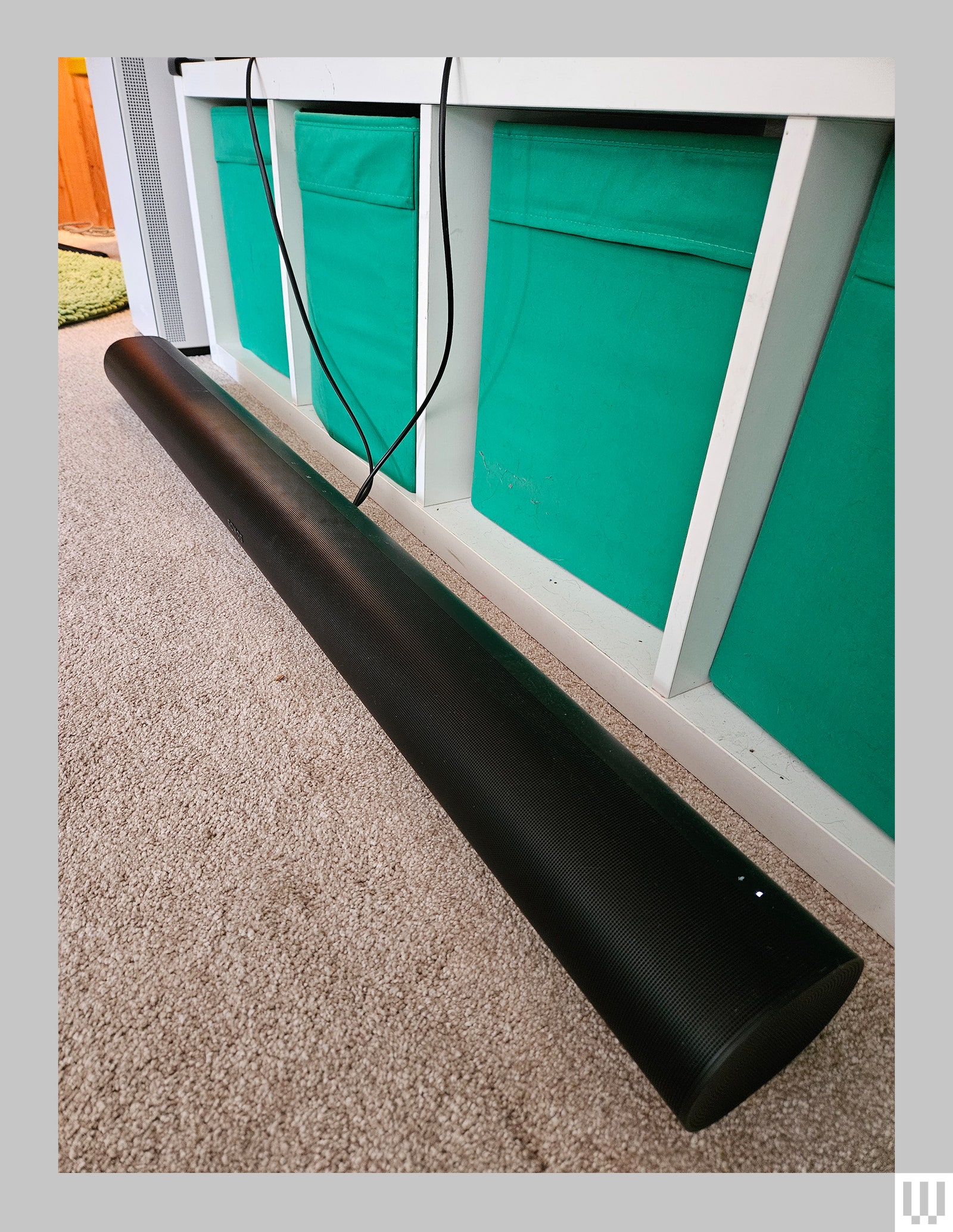 Black long tubeshaped speaker on the carpeted floor beside a credenza