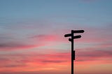 Direction signs in front of a sunrise sky.