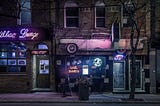 Picture of night scene: a bar at night — with a pink cadillac up top and dark city sidewalk area