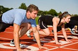 A man, a woman, and some other people outside of the camera frame, prepare themselves for a run on the racetrack.