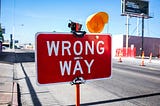 a wrong-way sign board on a road with a yellow light on it