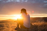 A woman sits within the rays of a sunset.