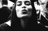 A black and white image of a graduate blowing a kiss at the photographer.