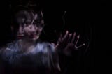 A blurry and distorted image of a woman reaching through the dark