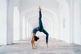 A woman doing a yoga pose in an empty hallway in an all-white building