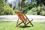 An empty orange and black stripped fold-up chair in a city park, waiting for someone to sit in it.