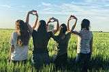 Four women standing in a field making hearts with their hands