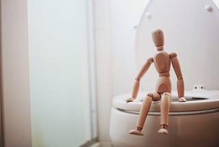 Small wooden toy doll sitting on toilet seat